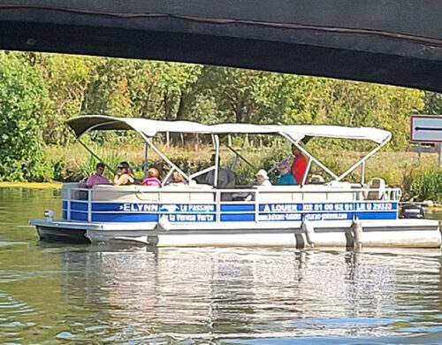 Pontoon boat with a white canopy carrying several passengers on a calm river, green trees in the background.0a0